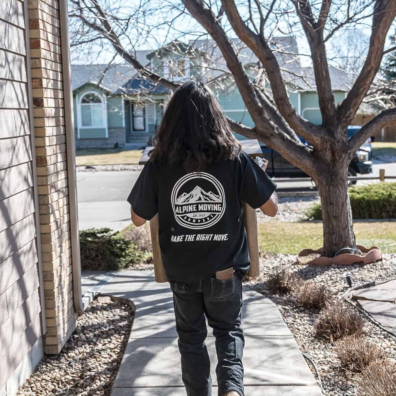 Person carrying box outdoors with moving company shirt.