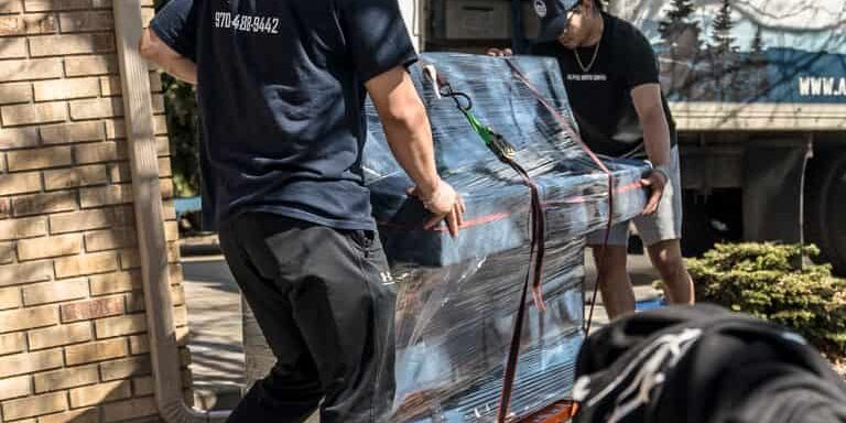 Movers transporting wrapped furniture with a dolly.