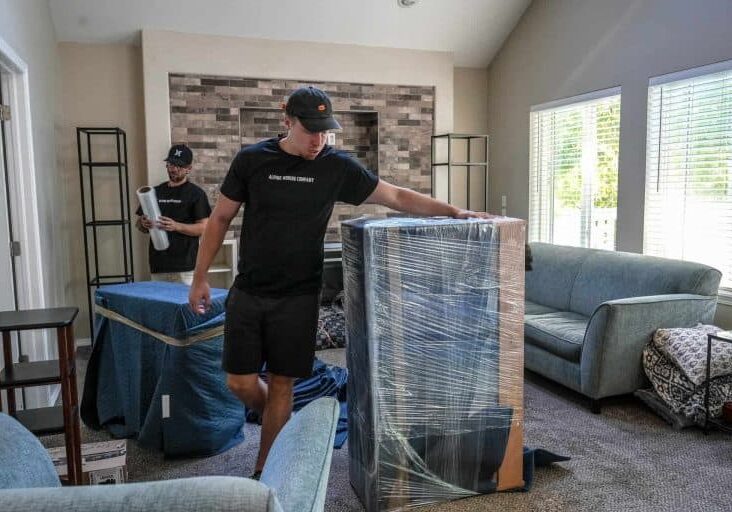 Movers wrapping furniture in living room.