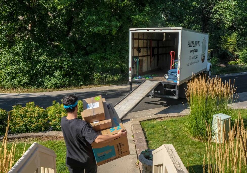 Person moving boxes into truck on driveway.