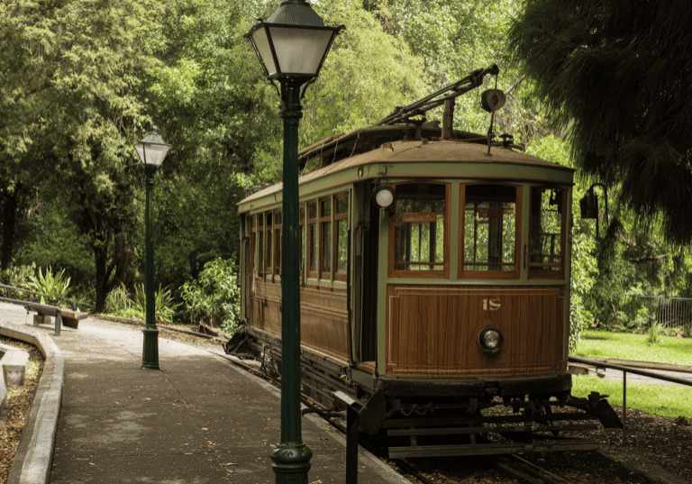 Vintage tram on a leafy track with lampposts.